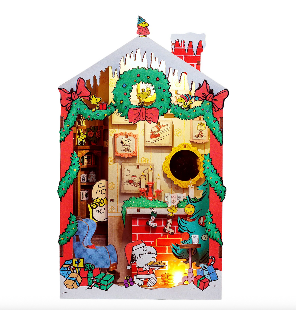 The Peanuts Christmas Miniature Book Nook Kit built to show the decorative Christmas scene with Snoopy as Santa Claus, Woodstock perched on a wreath and Sally and Charlie Brown peeking around the corner watching it all. 