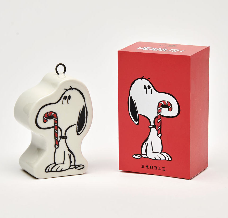 Snoopy with a candy cane bauble ornament sitting beside the red box with the illustrated image of the ornament on it. 