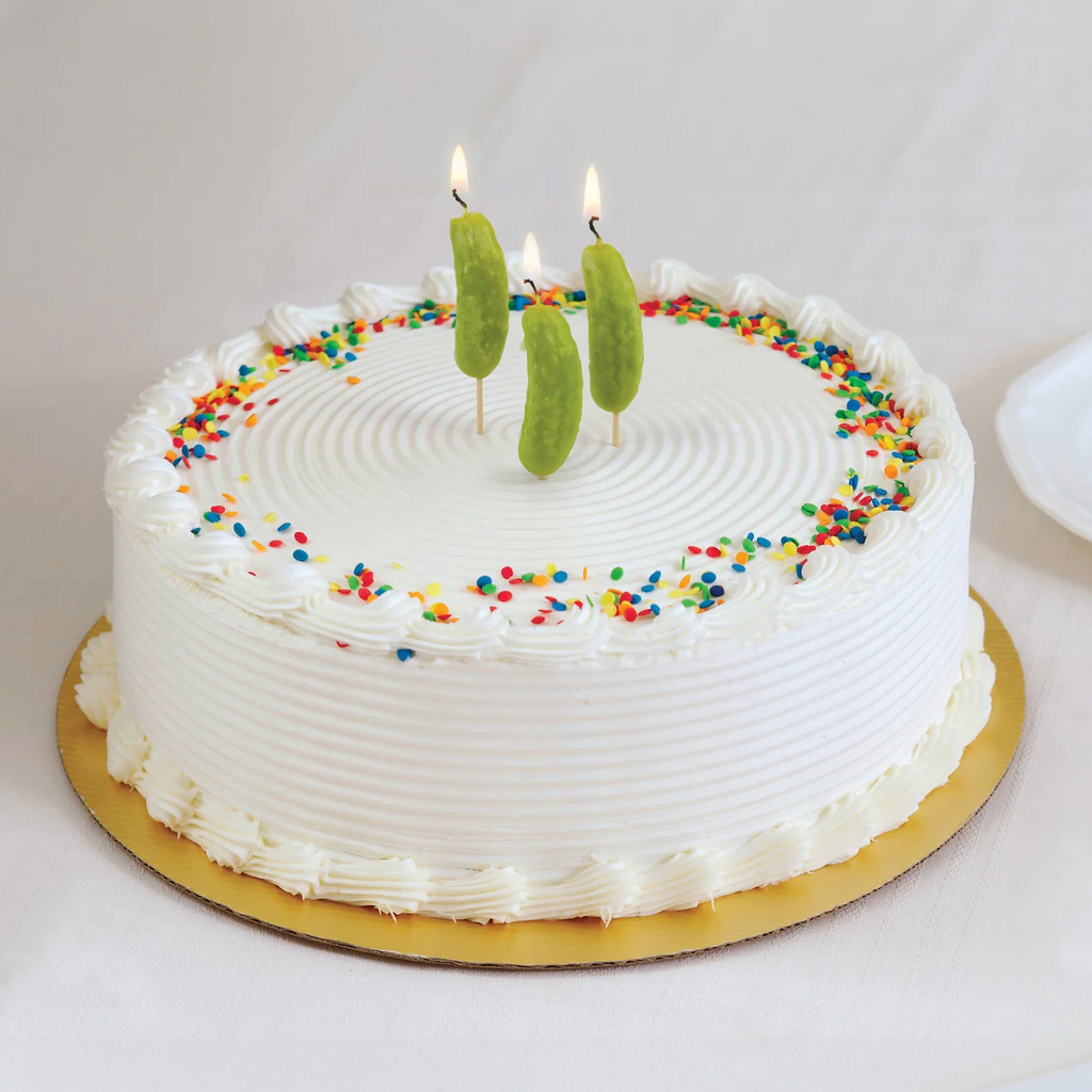 A beautiful cake with white icing and rainbow sprinkles topped with Pickle Party candles. 