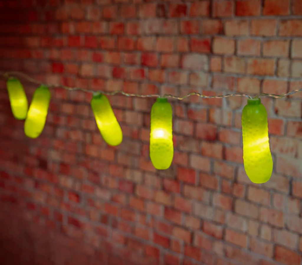 Pickle String Lights illuminated and hung up in front of a brick wall. 