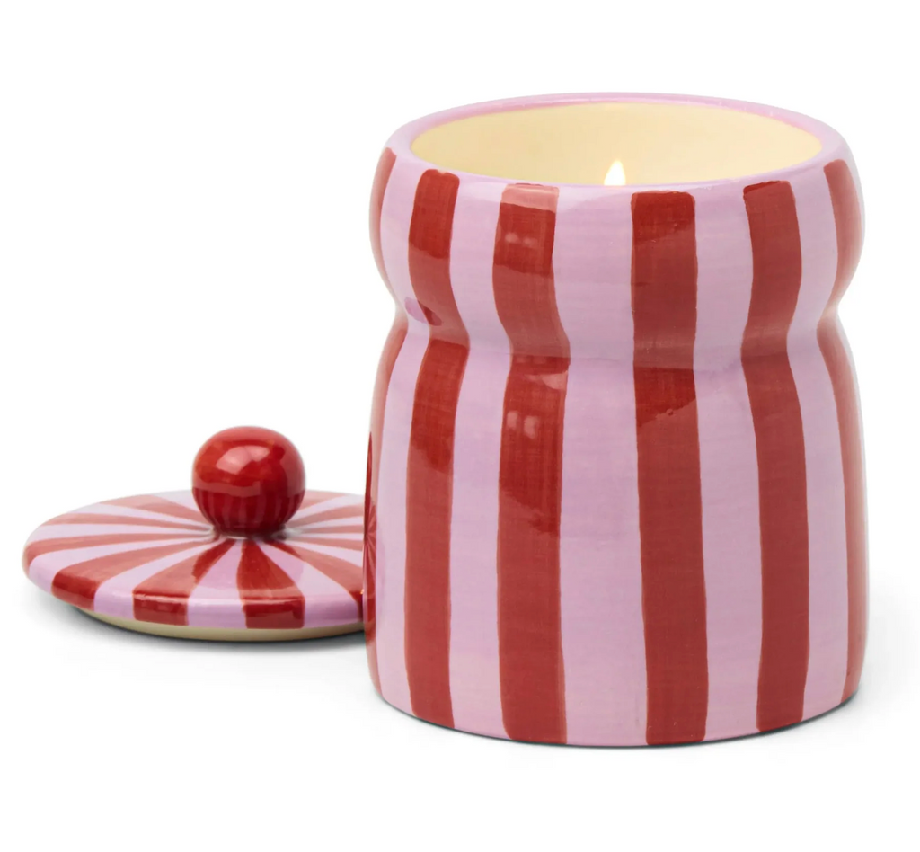Striped red and pink ceramic jar with a lit candle inside. 