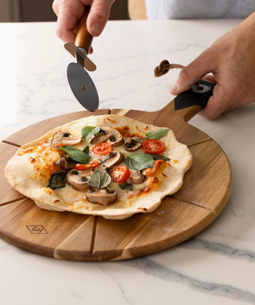 A small pizza on the cutting board with the pizza cutter about to use the grooves as guide to cut slices.