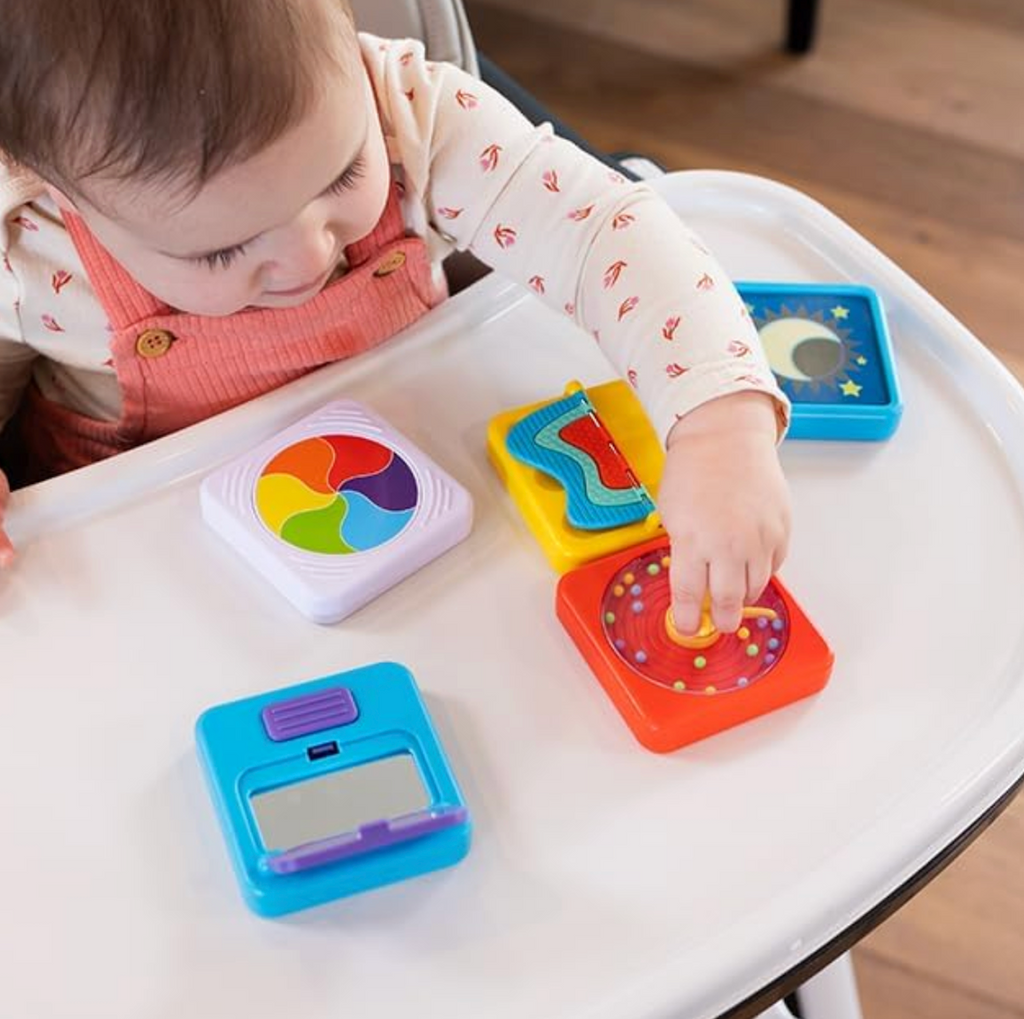 A toddler seated in a high chair with several of the Play Tab Sensory tiles placed on the table in front of them. 