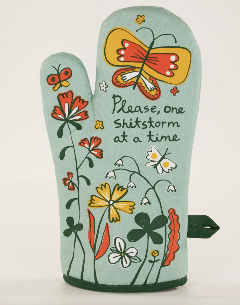Light blue oven mitt with illustrated flowers and butterflies that read "Please, one shitstorm at a time"