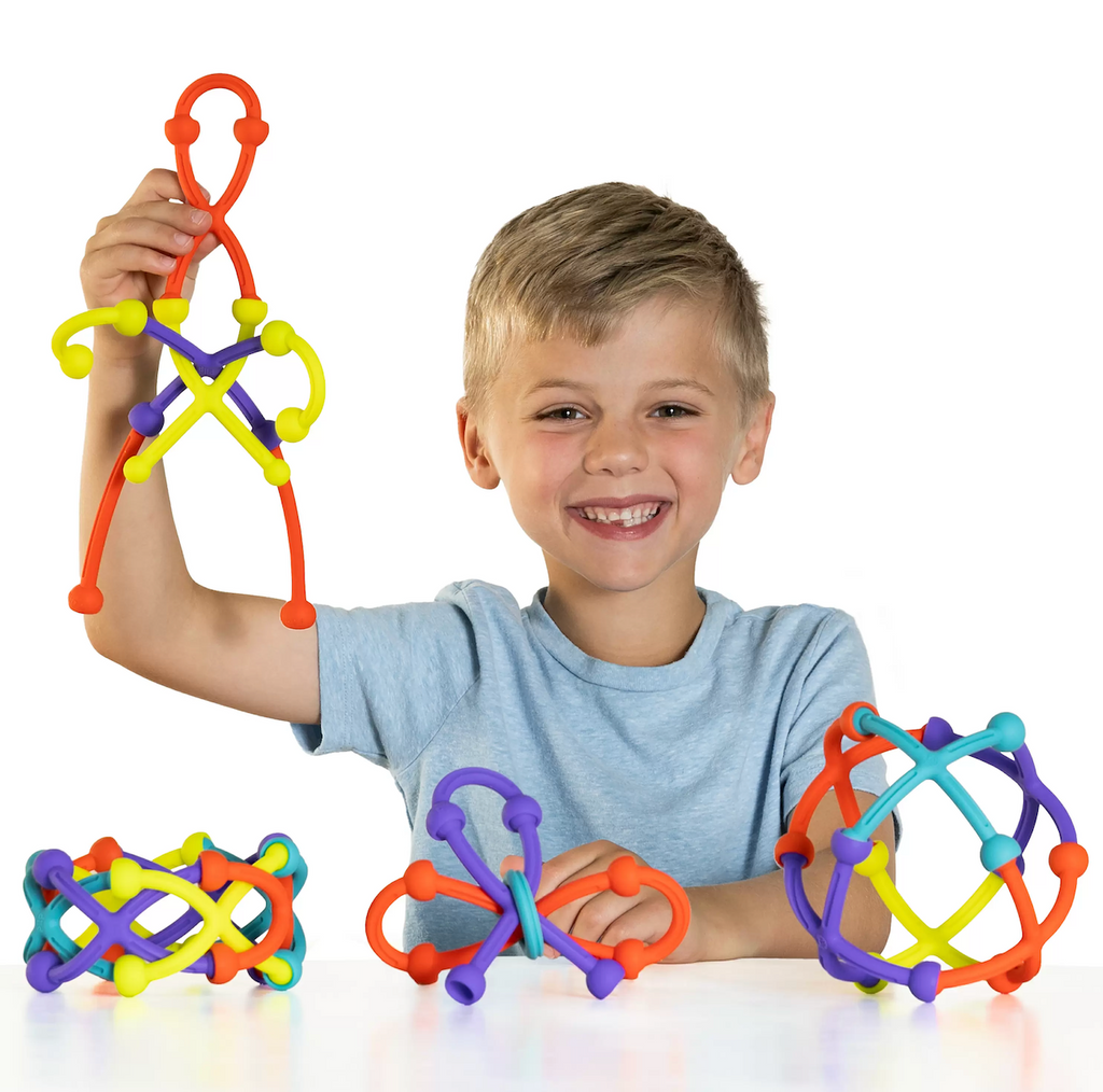 A young child holding up a creation made using the Plip Kit and various other creations on the table in front of him. 