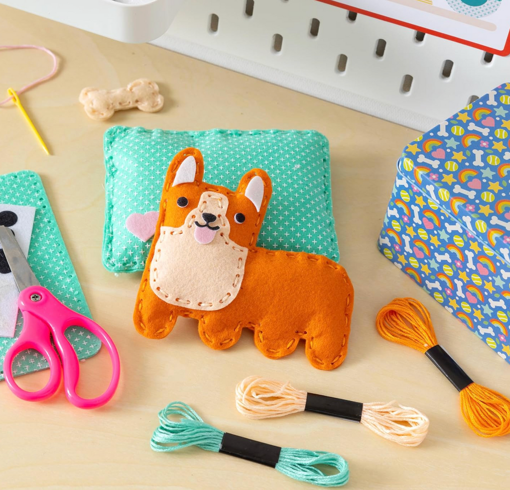 A little Corgi pocket pal sewn with the Pocket Pet Corgi Mini Craft Kit along with different colored threads, a plastic needle and scissors. 