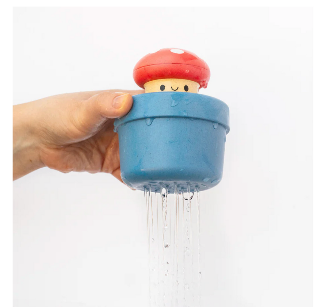 Hand holding a blue mushroom-shaped bath toy with water flowing out on a white background