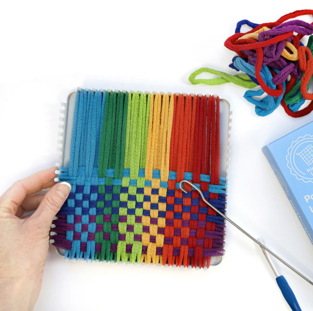 Colorful yarn loops woven on a metal loom with a hook used to weave the loops through each other. 