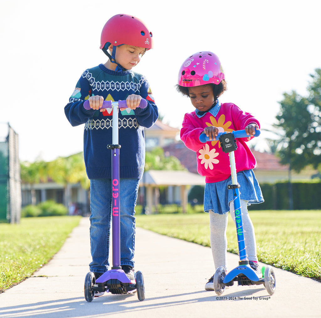 Two children riding their scooters in brightly colored clothing and safety helmets.
