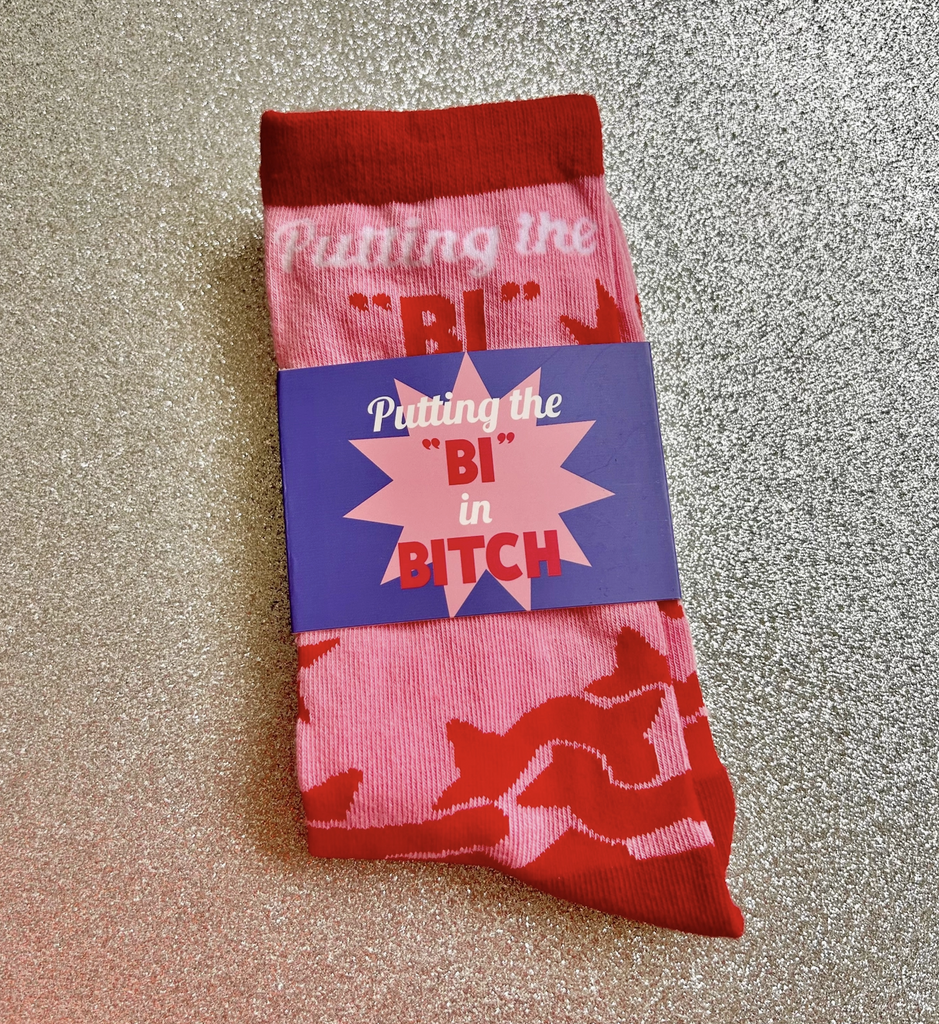 Pink socks with red designs folded to show the label that reads "Putting the "Bi" in Bitch"