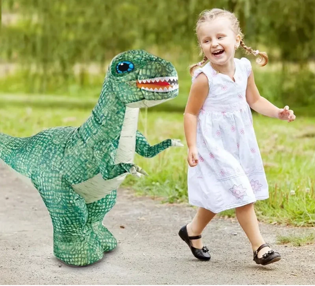 Child in a white dress running next to an inflated  green dinosaur rc toy outside.