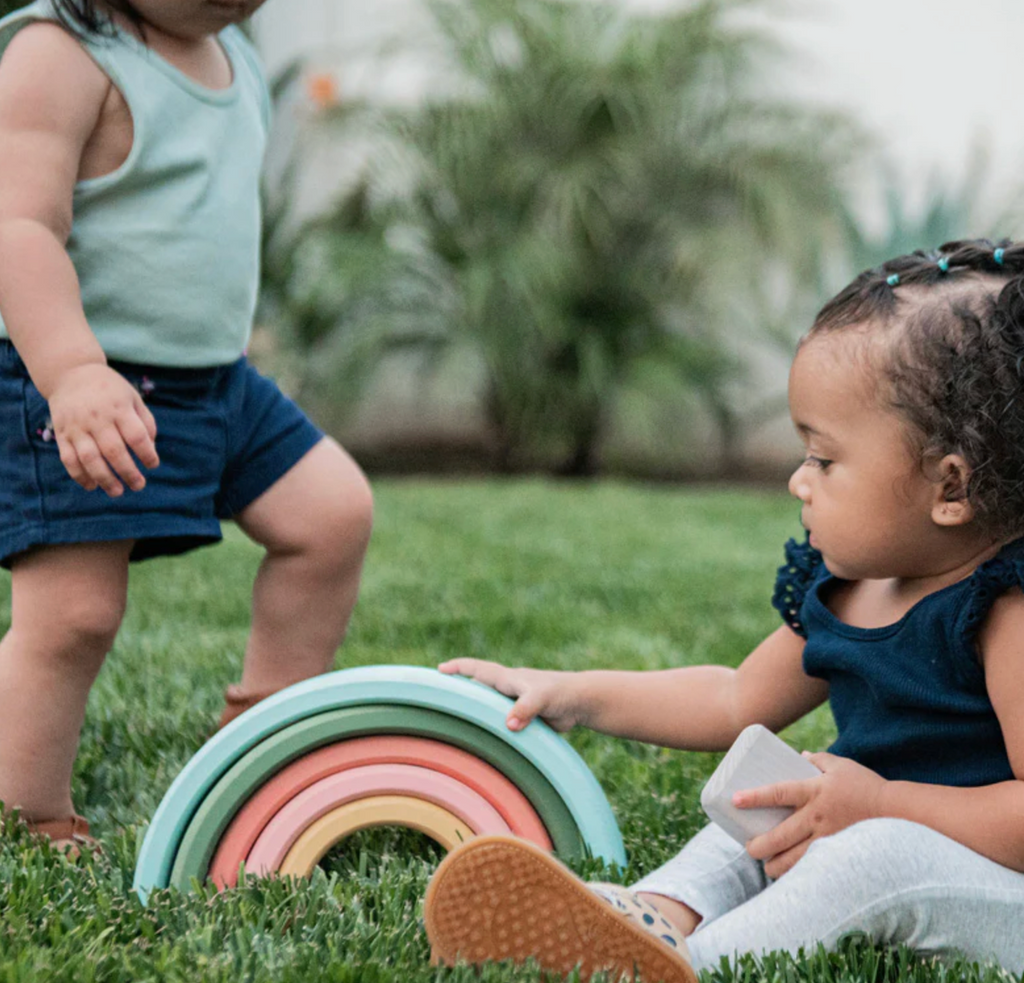 Two children playing with colorful wooden nesting pieces outside. 