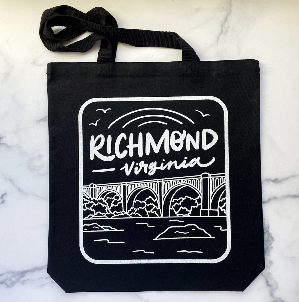 Black tote bag with a white screen printed design featuring a hand drawn rendition of the CSX A-Line Bridge over the James River, with hand lettered text that reads "Richmond, Virginia."