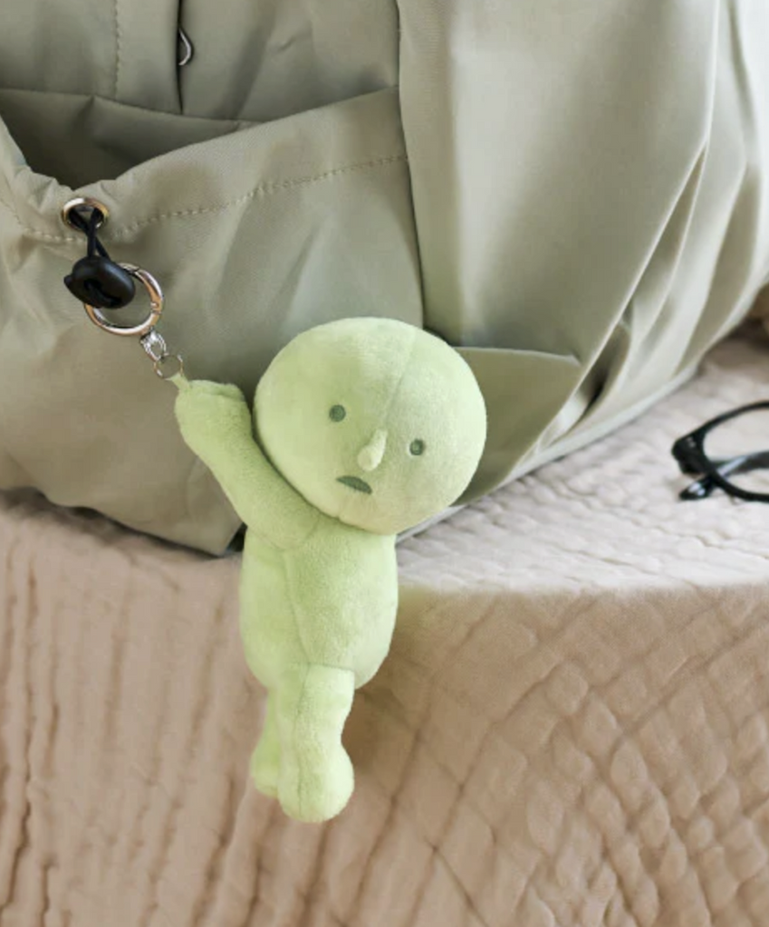 Green plush Smiski Hanging On keychain attached to a bag. 