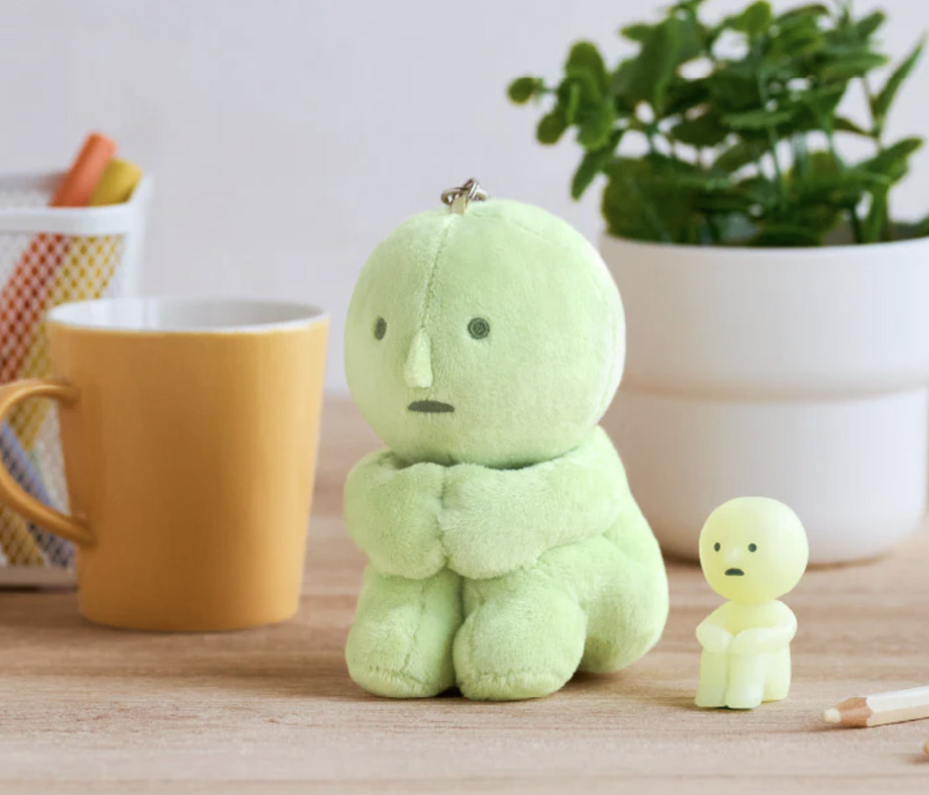 Green , plush Smiski in the "hugging knees" pose with a silver key ring attached at the top.  