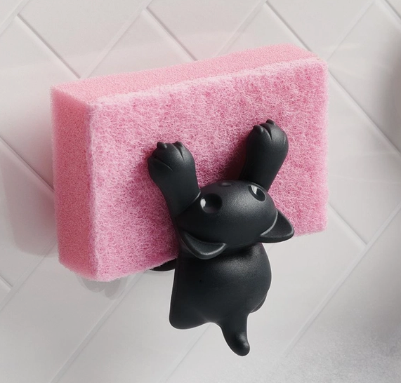 Scrubby the black cat sponge holder suctioned to a wall holding a pink sponge. 