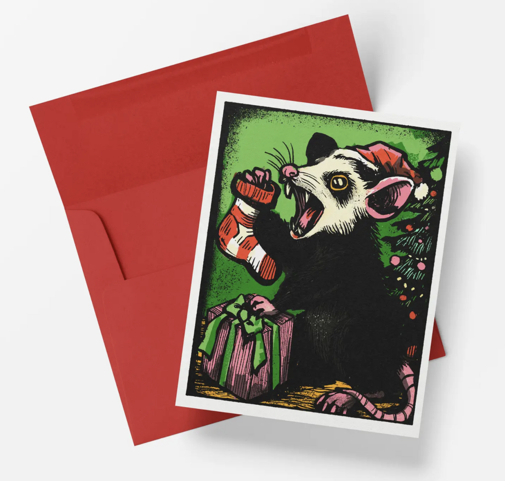 Christmas card features a possum in a Santa hat holding a striped stocking in front of a Christmas tree.