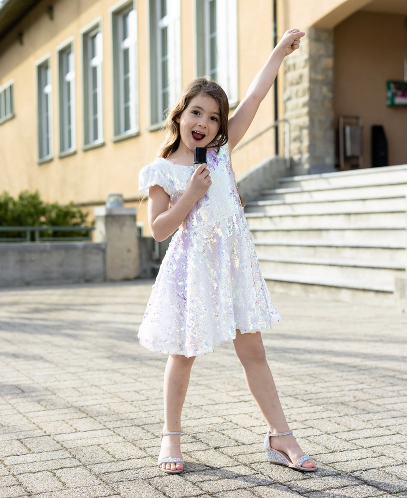 A young girl wearing the Sequins Concert Queen Dress with sparkly shoes to match, holding a microphone and belting out a favorite tune. 