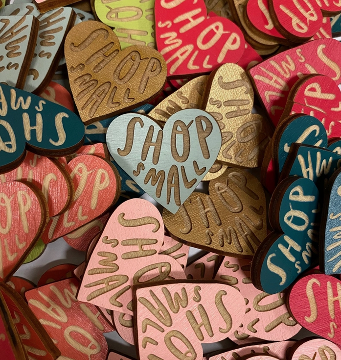 Assorted colors of the heart shaped wooden pin that reads "Shop Small"
