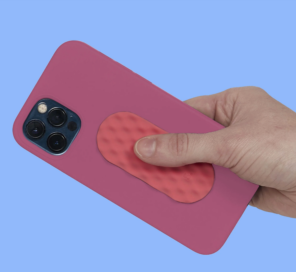 A hand holding a smart phone with a Mesh Oval sensory sticker attached to the back of it. 