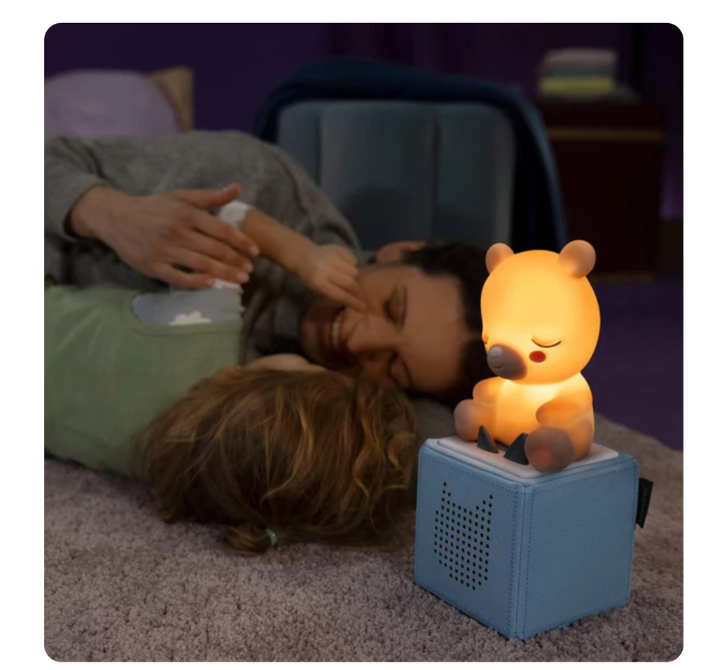 Sleepy Bear Night Light glowing on top of a blue Tonies Box while a parent and child cuddle nearby.