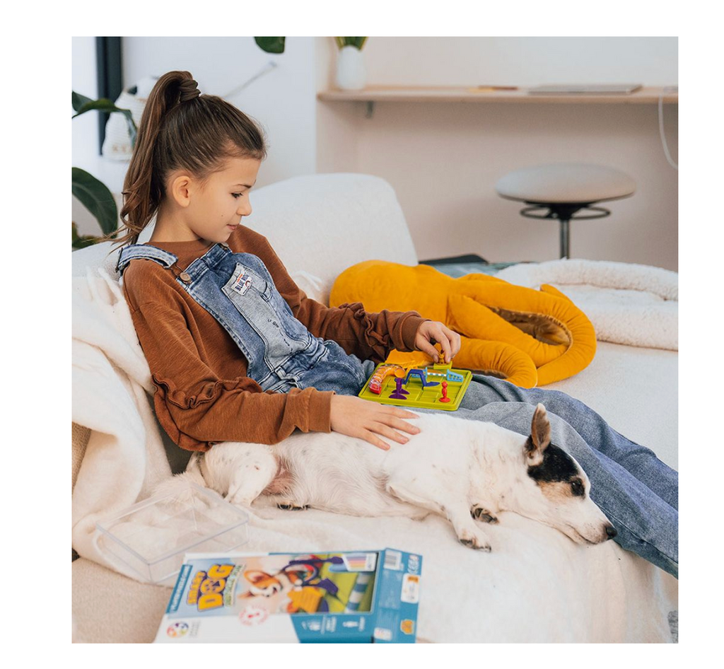 Young girl sitting on a white couch playing the Smart Dog game with a dog sleeping next to her.