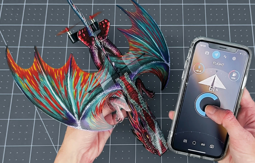 The PowerUp Dragon assembled with colorful pre-cut paper and a hand holding a smartphone ready to control it's flight. 