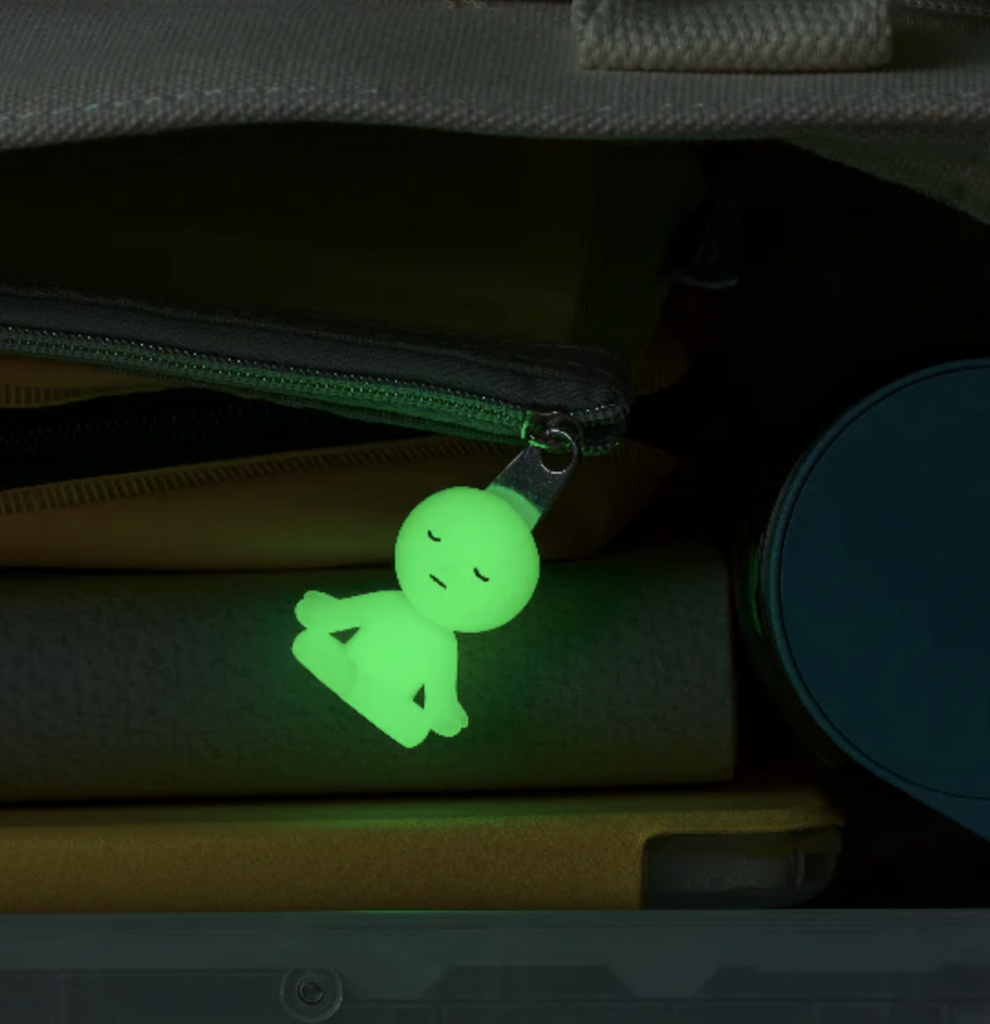 Smiski Zipper Bite attached to a zipper on a backpack, brightly glowing in the dark. 