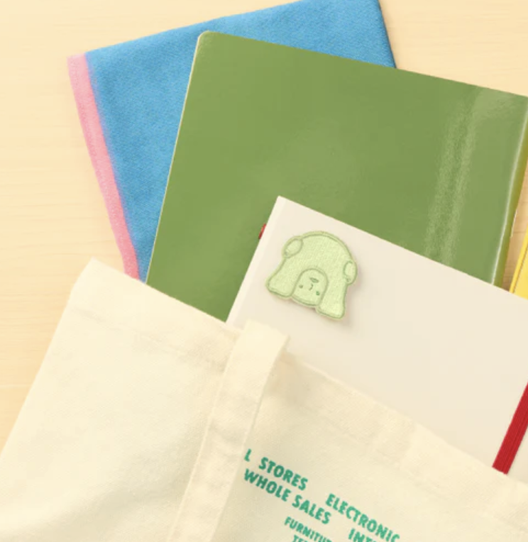 Smiski Peeking embroidered sticker on a stack of books.