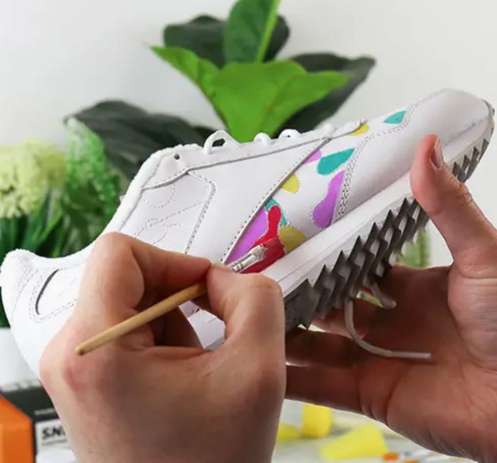 A picture of a pair of sneakers being painted with bright colors. 