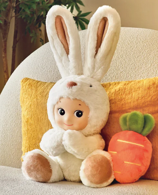 The Sonny Angel Cuddly Rabbit sitting on a couch with it's carrot beside it. 