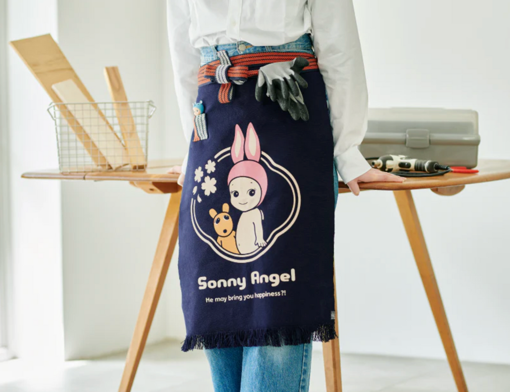 Person leaning on a wooden desk wearing the Sonny Angel maekake apron.