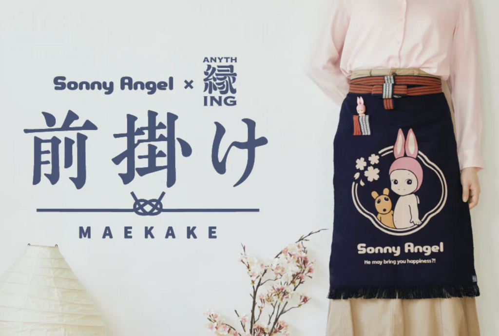 Person wearing blue Sonny Angel maekake apron standing next to cherry blossoms in front of a white wall.