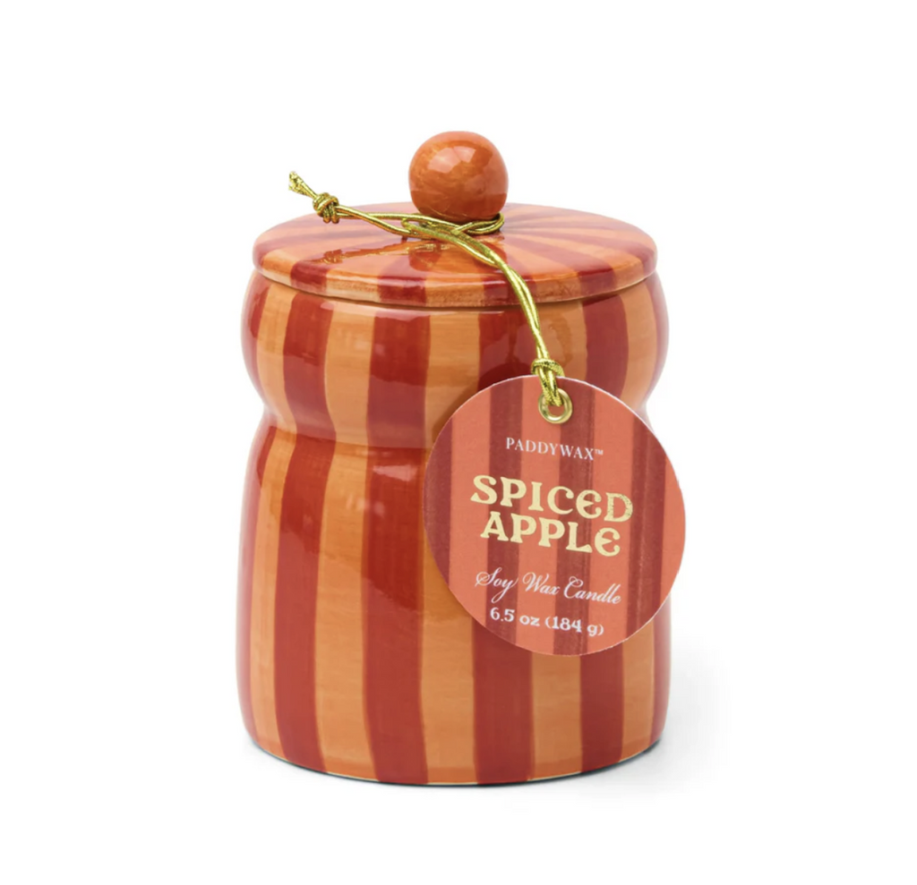 Spiced Apple cabana ceramic candle. Housed in a hand-painted orange and red vessel with a matching lid. With an orange and red striped tag that reads "Spiced Apple Soy Wax Candle" hanging from the lid. 