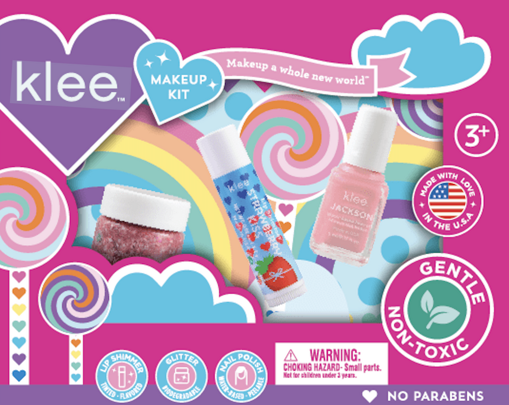 Bright pink box with colorful swirly lollipops decorating the box. The center has a clear plastic window that shows the light pink nail polish, strawberry kiss lip shimmer, and jar of pink body glitter. 