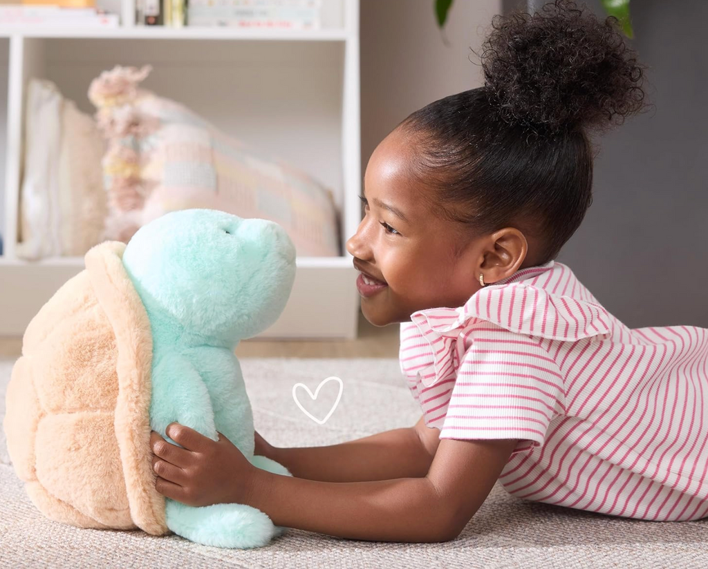 A young child laying on the floor holding Sprout the Sea Turtle. 