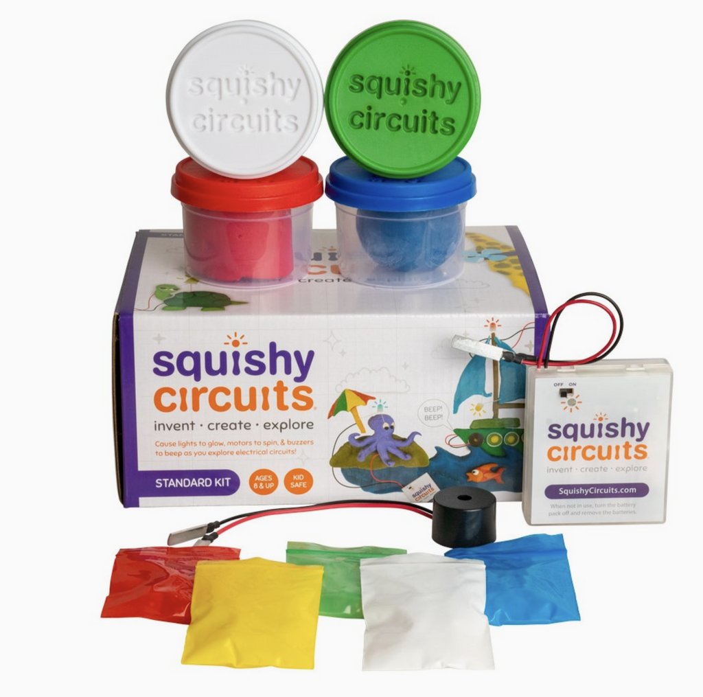 Components of the Squishy Circuits Standard Kit, Four colors of play dough white, green, blue and red stacked on top of the box in clear containers. There is also a battery pack, a piezoelectric buzzer, and LEDs in Red, Green, White, Yellow, Blue. 