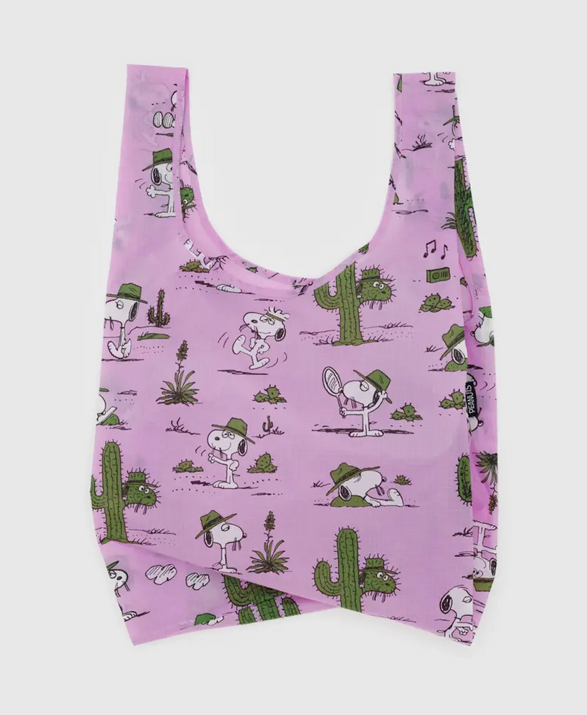 The Standard Baggu reuseable bag with Snoopy in various poses wearing a green fedora amongst large cactus on a lilac background.