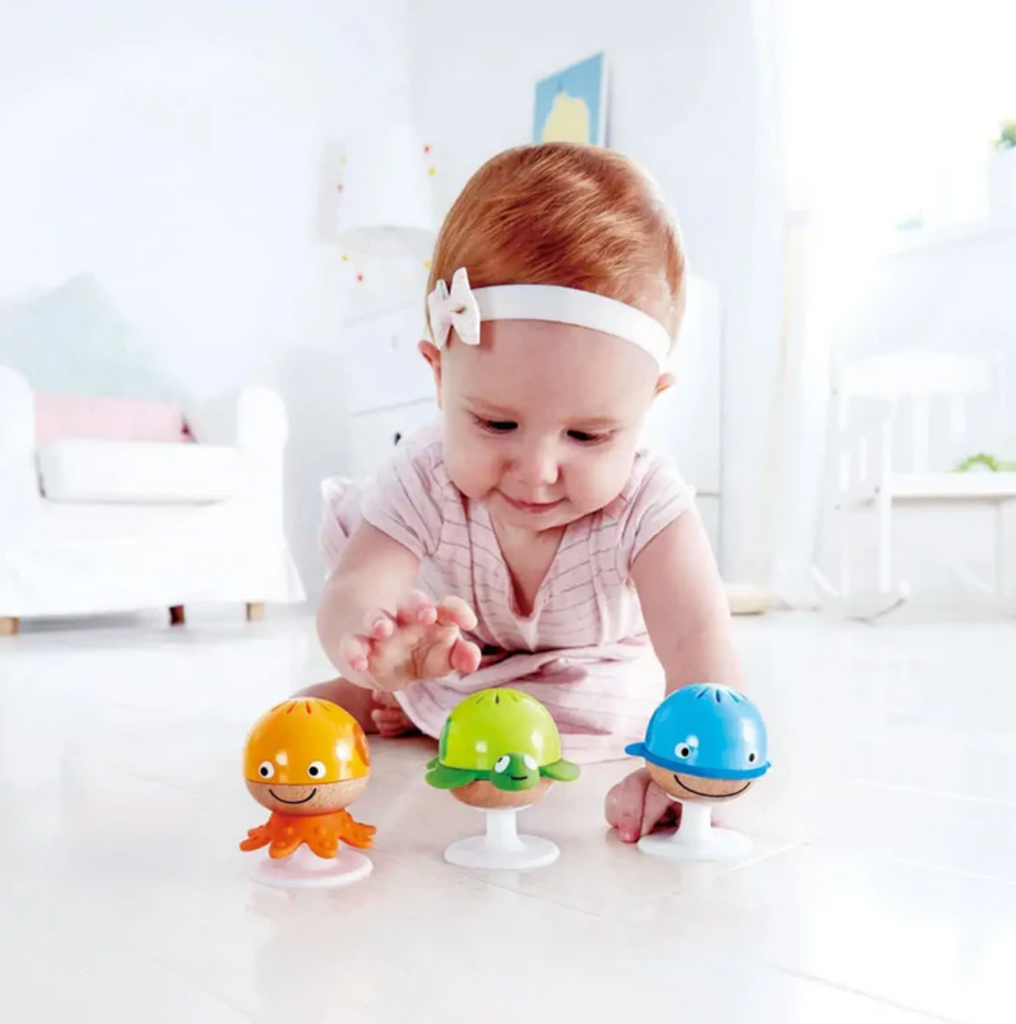 A baby playing with the Stay Put Rattle set which are suctioned to the floor to make play easy and exciting. 
