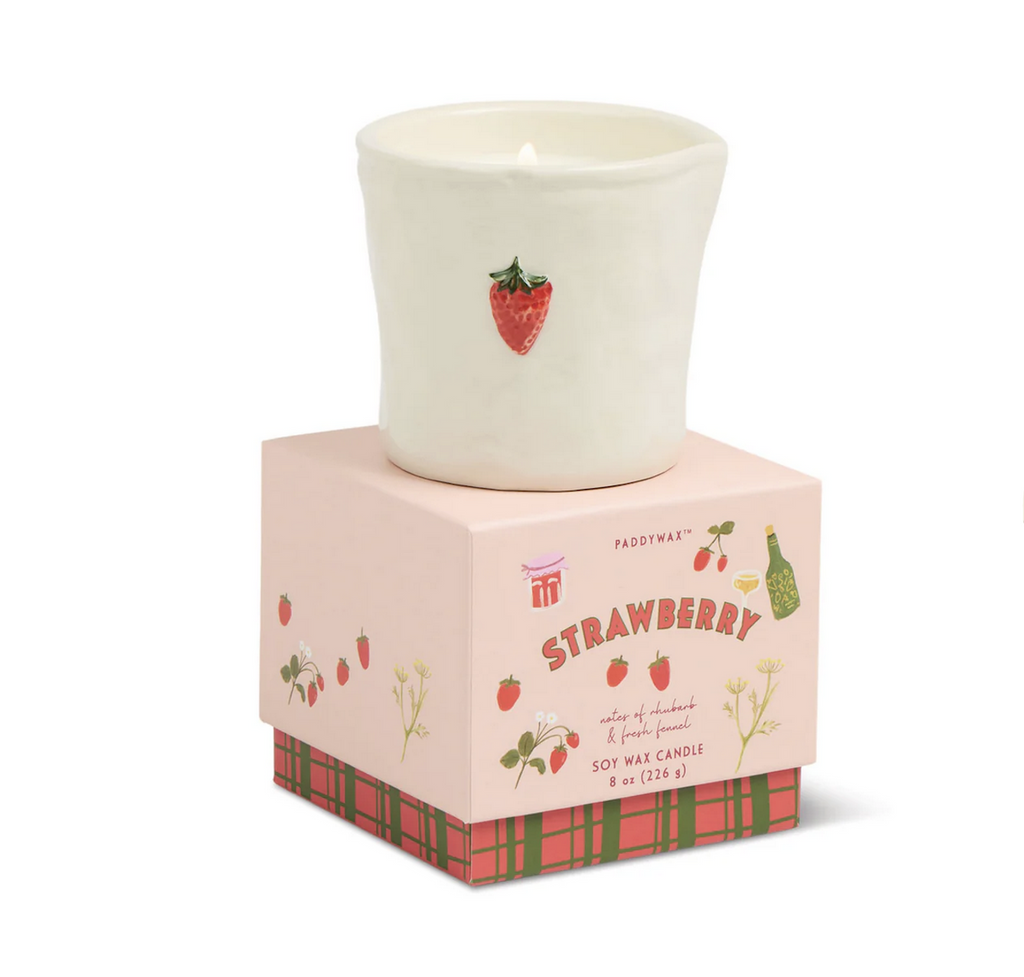 Strawberry Bistro Candle from Paddywax packaged in a beautiful gift box adorned with strawberries and blossoms. The candle is sitting on top of the box in a reusable ceramic vessel featuring a hand painted strawberry on the front. 