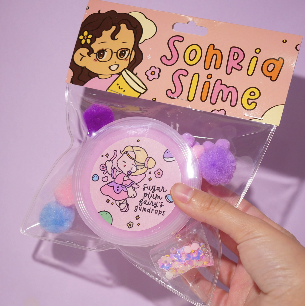 Sugar Plum Fairy's Gumdrops Slime by Sonria Slime in a clear package with a bag of iridescent sequins to mix into the slime and purple, pink and blue pom poms. (Not food)