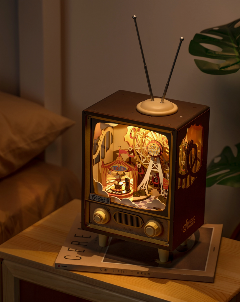 Sunset Carnival DIY Mechanical Music Box lit up sitting on a side table in a darkened bedroom.