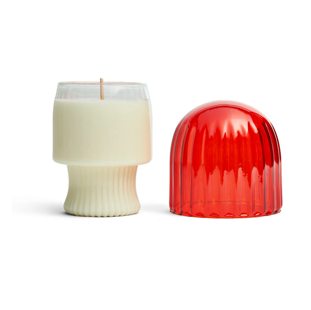 White candle in a clear glass holder next to its orange mushroom shaped top.