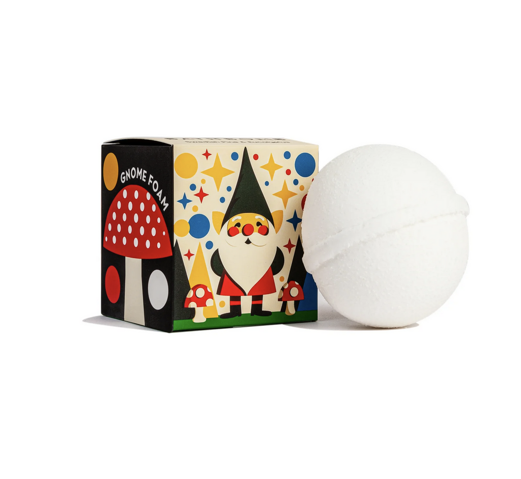 White foaming bath bomb next to box illustrated gnome standing next to tiny mushrooms.