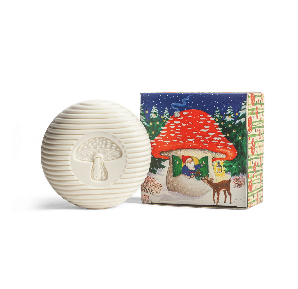 White soap embossed with a mushroom ext to illustrated box with a gnome looking out the window of their mushroom house, feeding a deer.