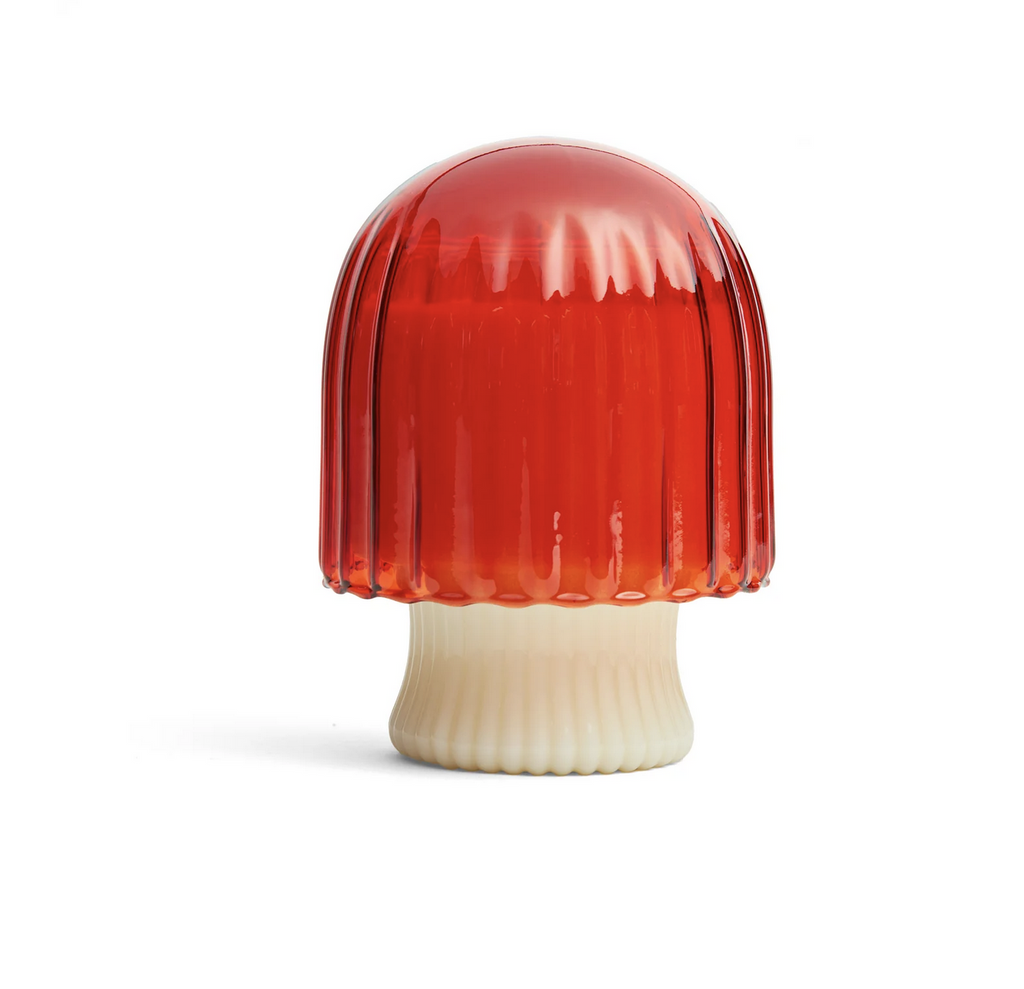 Candle in a glass holder with an orange mushroom shaped top.