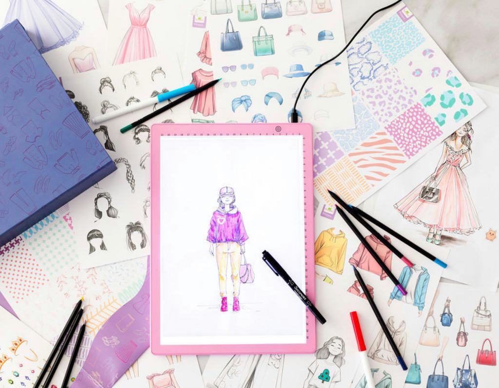 LED lighted pad with a fashion drawing on it with other drawings of handbags, jackets and all sorts of fashionable attire scattered around. 