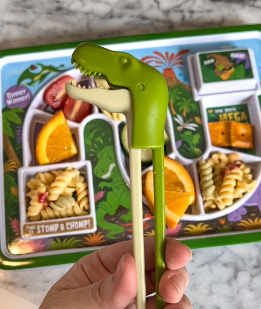 T-Rex head connecting green chopsticks, held over a kids dino themed plate. 