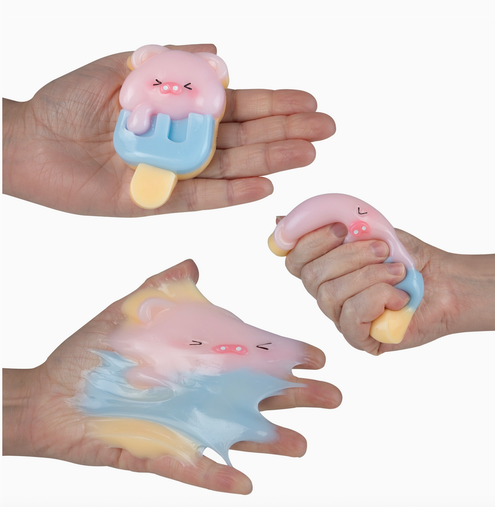 Squishy toy shaped like a piggy ice cream bar being squished by hands on a white background
