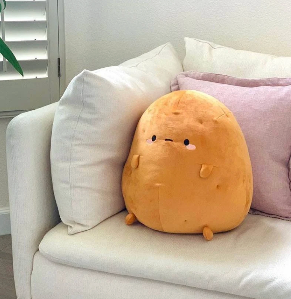 Tayto Potato Mochi Plush nestled on a couch amongst pillows. 